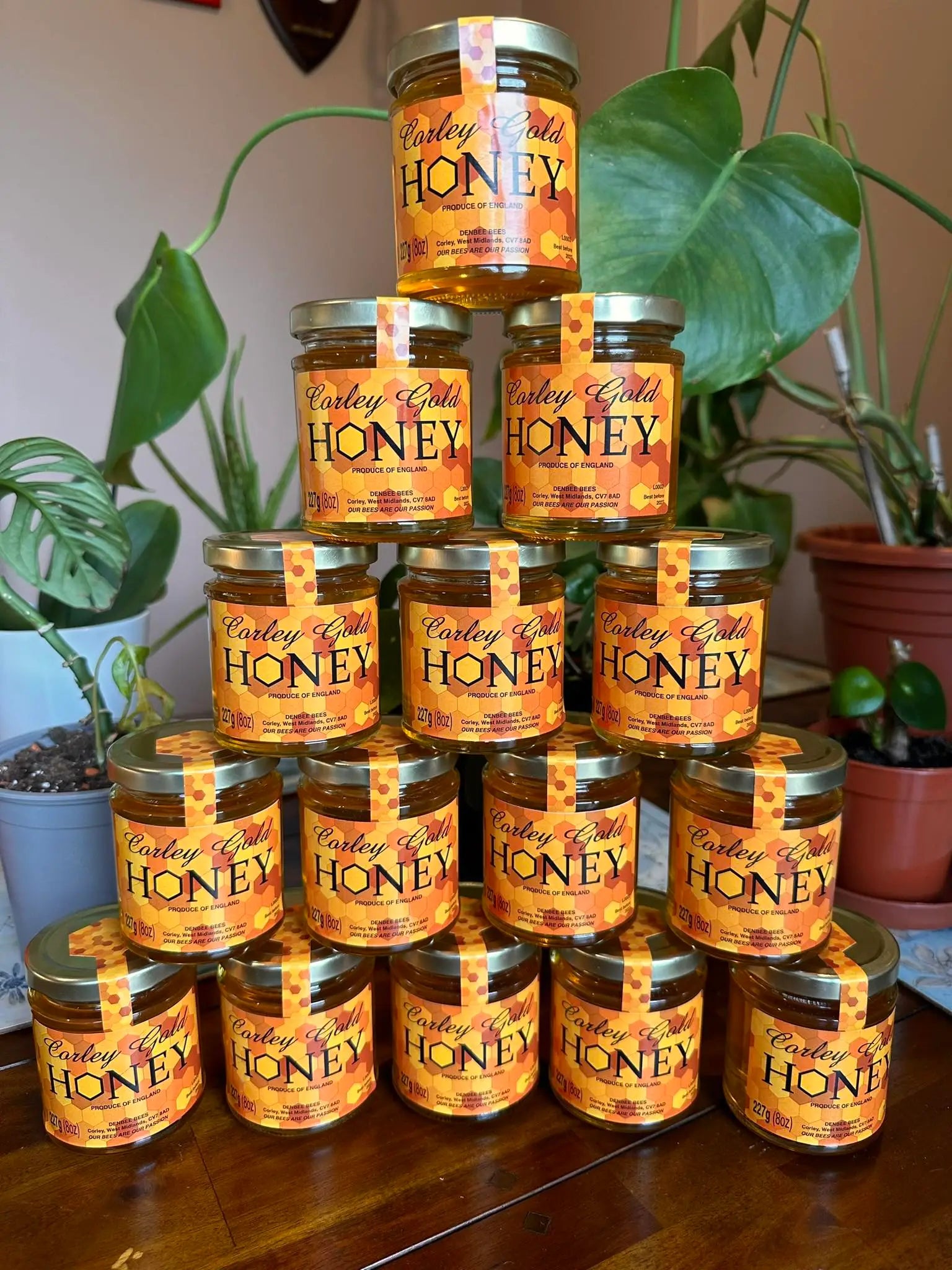 Stack of Corley Gold Honey jars on a wooden surface with plants in the background